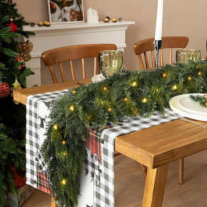 Decorated dining table with Christmas garland, lights, and checkered tablecloth.